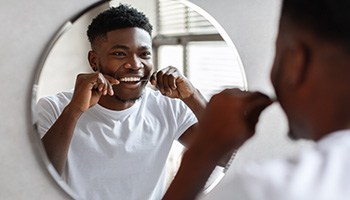 Man smiling while flossing his teeth in bathroom