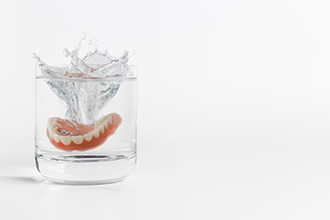 Full set of dentures splashing into a glass of clear liquid with a white background