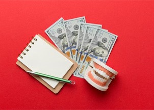 Notepad, money, and dental model against red background