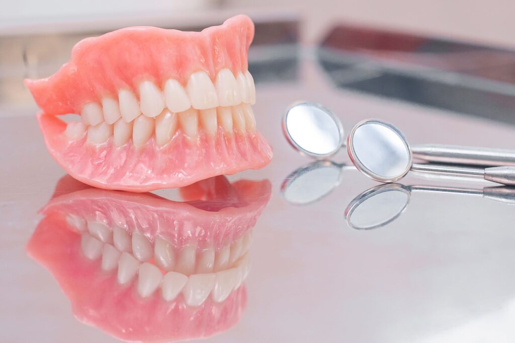 Full set of dentures on reflective surface next to two dental mirrors